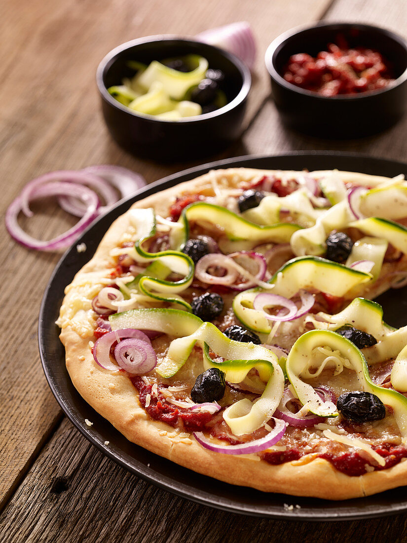 Pizza mit Zucchini, roten Zwiebeln und schwarzen Oliven